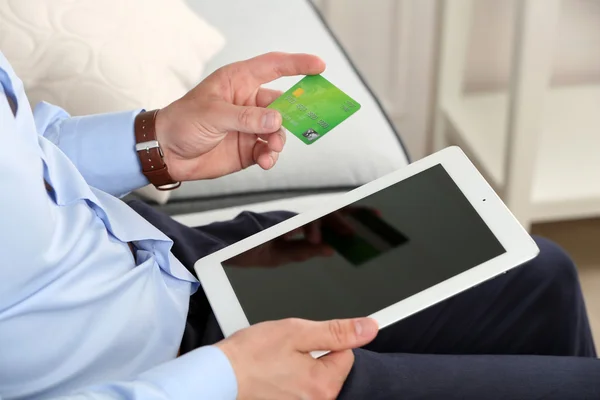 Man holding credit card and tablet on sofa in room