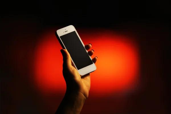 Female hand with mobile phone on blurred night lights background