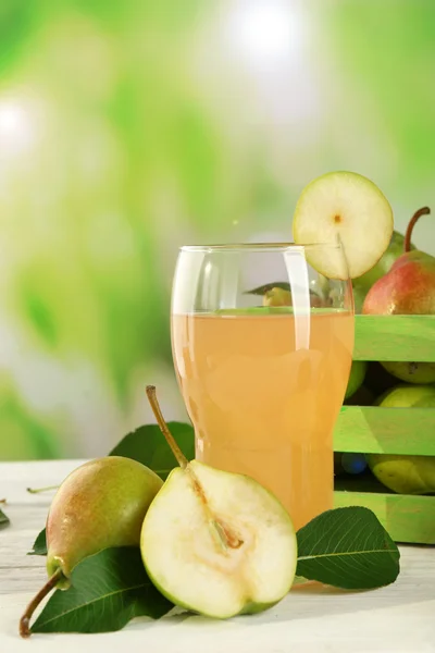 Glass of juice with fresh pears on wooden table on blurred background