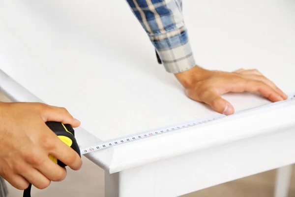 Young man measuring home furniture with measure tape, close up