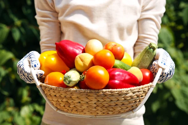 Woman holding basket with fruits and vegetables outdoors