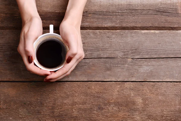 Female hands holding cup of coffee on wooden background