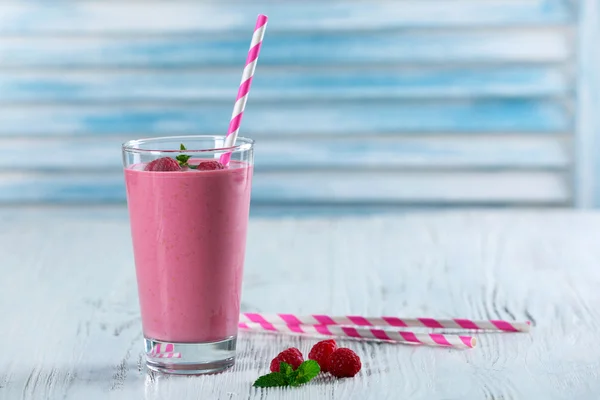 Glass of raspberry milk shake with berries on wooden background
