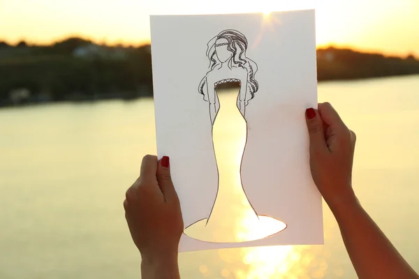 Drawing woman in cutout dress on sheet of paper on nature background