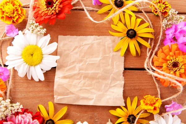 Fresh colorful flowers with crumpled sheet of paper on wooden table, top view