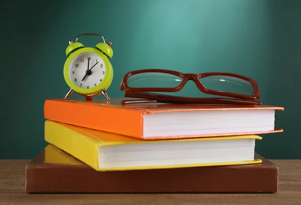 Stack of books with glasses and alarm clock on desk on green chalkboard background