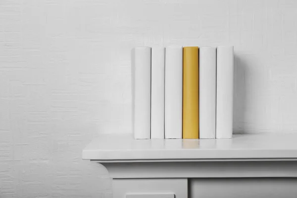 Blank books and yellow one on shelf on white wallpaper background