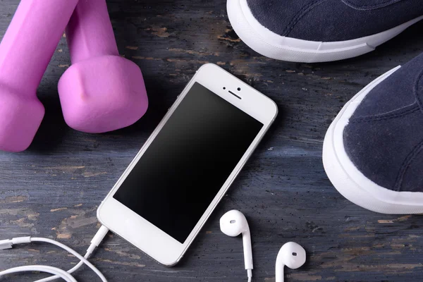 Mobile phone and earphones with set for sports on wooden table, closeup