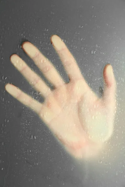 Female hand behind  wet glass