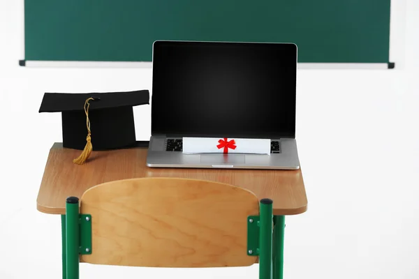 Laptop, master hat and diploma on table