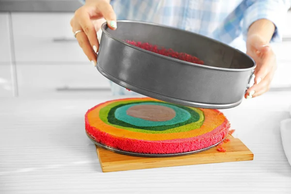 Young woman making rainbow cake in kitchen