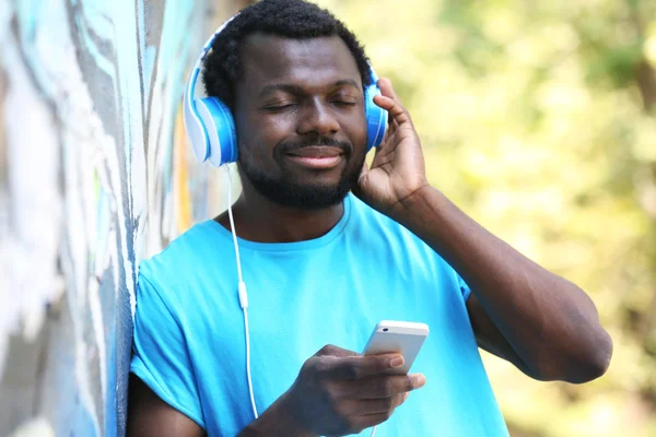 African American man listening music with headphones near graffiti wall outdoors