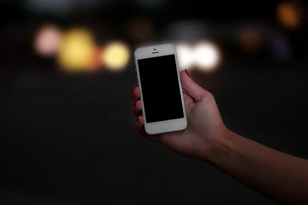 Female hand with mobile phone on blurred night lights background