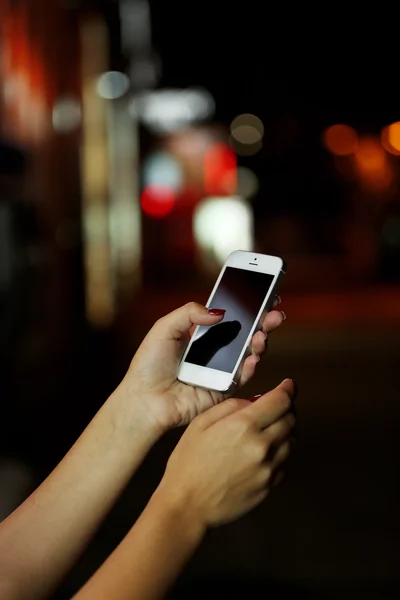 Female hand with mobile phone on blurred night lights background