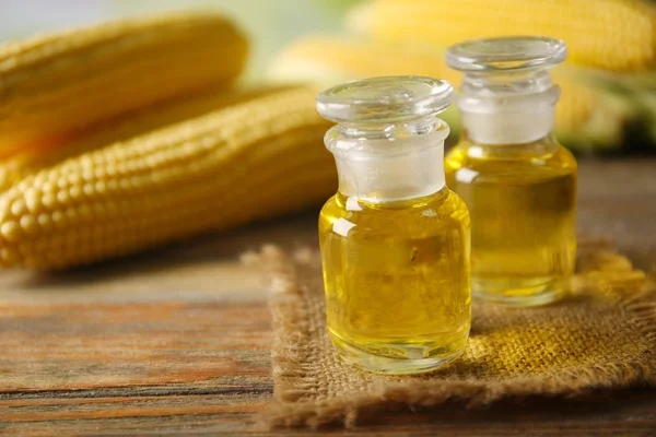 Fresh corn with bottles of oil on table close up