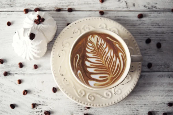 Cup of coffee with beans and zephyr on wooden table, top view