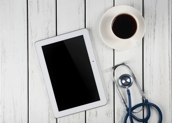 Blank tablet, stethoscope and cup of coffee on wooden background