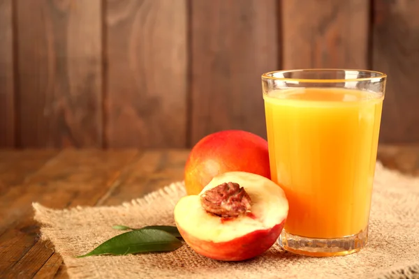 Ripe peaches and glass of juice on wooden background