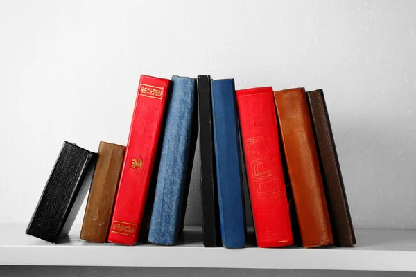 Old books on shelf, close-up, on light wall background