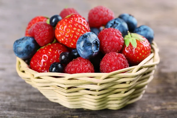 Sweet tasty berries in basket on wooden table close up