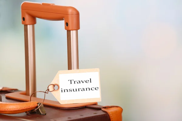 Suitcase with TRAVEL INSURANCE label on light blurred background