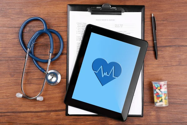 Stethoscope with pills and digital tablet on wooden background