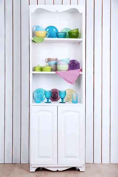 Clean glasses, plates and cutlery on shelves in kitchen cupboard