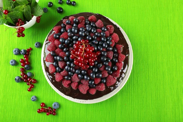 Delicious chocolate cake with summer berries on green tablecloth, top view