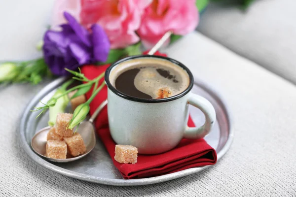 Cup of coffee with flowers on tray on sofa in room