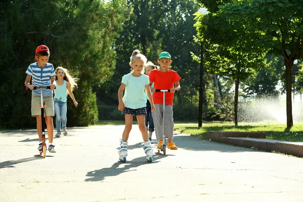 Children riding on scooters and roller skates in park