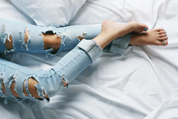 Woman in blue jeans on bed top view