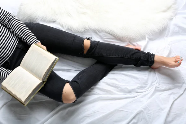 Woman in black jeans reading book on bed top view point