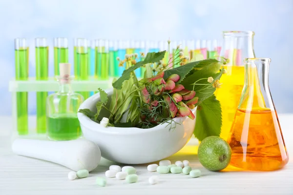 Herbs in mortar, test tubes and pills, on table, on light background