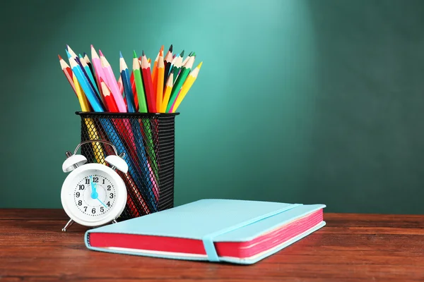 Notebook, metal cup of crayons and alarm clock