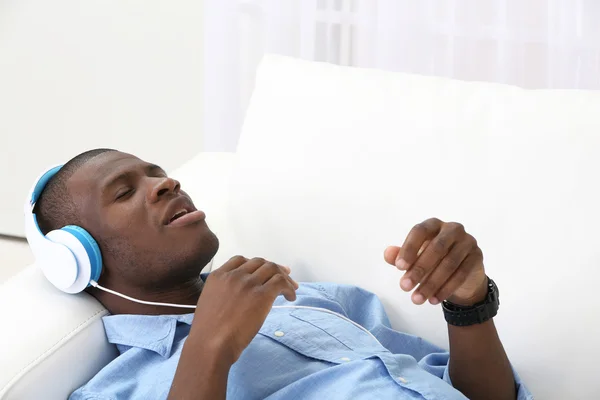 Handsome African American man with headphones lying on sofa close up