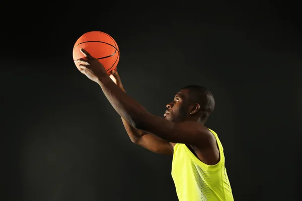 African American basketball player holding ball on dark background