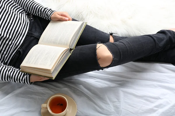 Woman on the bed with old book and cup of coffee