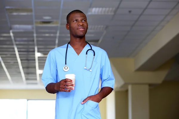 Handsome African American doctor holding cup of coffee in hospital
