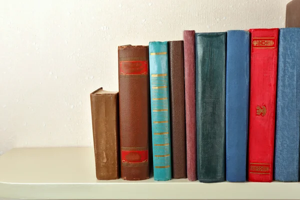 Old books on shelf, close-up, on light wall background