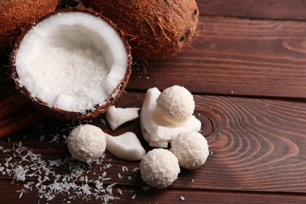 Candies in coconut flakes and fresh coconut on dark wooden background