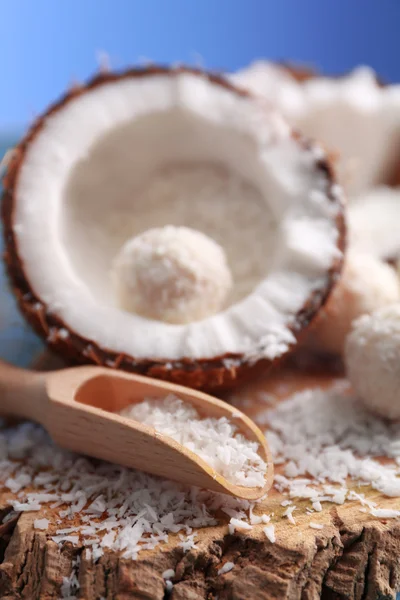 Candies in coconut flakes and fresh coconut on color wooden background