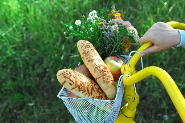 Young woman driving bike with basket of fresh foodstuffs, close-up