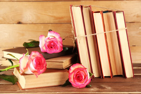 Tied books with pink roses on wooden background