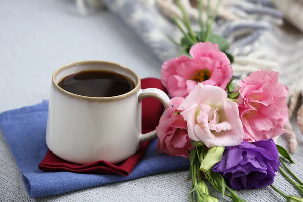 Cup of coffee with flowers near books on sofa in room