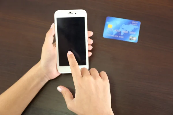 Woman verifies account balance on smartphone with mobile banking application on wooden table background