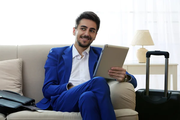 Business man with suitcase and tablet sitting on sofa at home