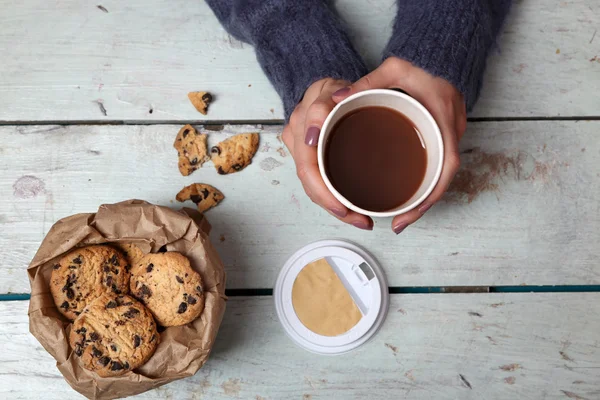 Hands holding cup of coffee and cookies