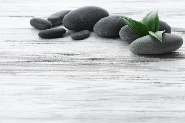 Spa stones with green leaves on wooden background