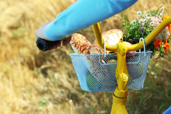 Young woman driving bike with basket of fresh foodstuffs, close-up
