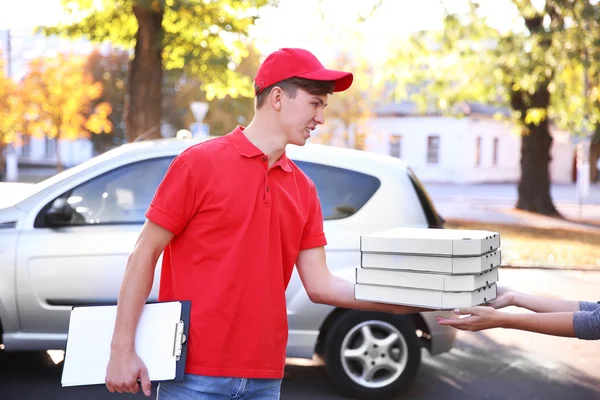 Pizza delivery boy holding boxes with pizza near car